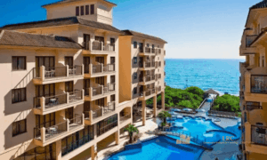 Piscina de resort pé na areia integrada à arquitetura do Jurerê Beach Village com vista do mar ao fundo.