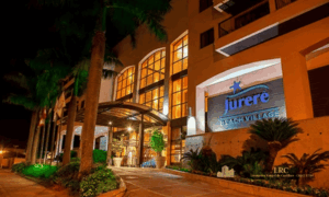 Fachada iluminada à noite do Jurerê Beach Village com letreiro principal destacado.