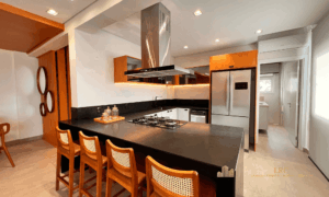 Cozinha americana gourmet na cobertura duplex Cachoeira Boulevard com ilha central, coifa de inox e banquetas de palha.