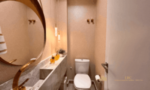 Lavabo social moderno com bancada de mármore, cuba esculpida, torneira dourada e espelho iluminado.