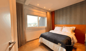 Suíte master da cobertura duplex Cachoeira Boulevard com cama de casal decorada de frente para o janelão com vista mar.