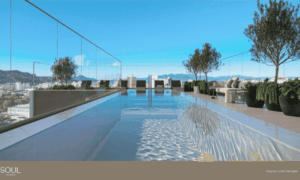 Perspectiva da piscina externa do Soul Wkkoerich de raia localizada no terraço (rooftop). O ambiente possui espreguiçadeiras, plantas ornamentais em vasos pretos e uma barreira de vidro que permite visualizar o skyline do Centro e o mar ao fundo.
