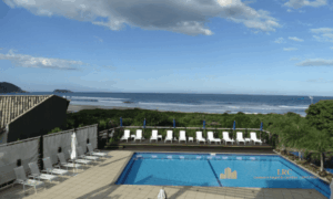Espaço de relaxamento no jardim com quiosque de sapé e vista para a praia.