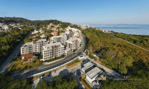 Vista aérea diurna mostrando a implantação das 5 torres do empreendimento próximas ao mar e à área verde.